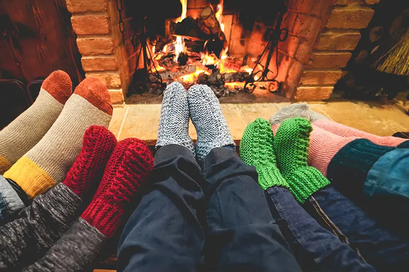 Feet with holiday socks propped up on a table near a fireplace