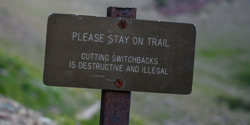 A trail sign that reads: Please stay on trail. Cutting switchbacks is destructive and illegal. A trail sign that reads: Please stay on trail. Cutting switchbacks is destructive and illegal.